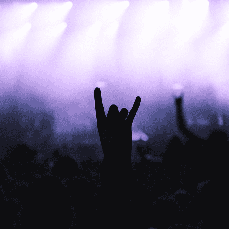 Konzertpublikum mit erhobener Hand im Rock-Gruß vor lila Bühnenlicht – Symbol für Energie, Leidenschaft und Live-Musik.