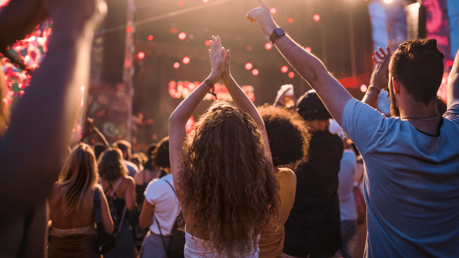 Jubelndes Publikum bei einem Live-Konzert mit erhobenen Händen, warmem Bühnenlicht und ausgelassener Festivalstimmung.